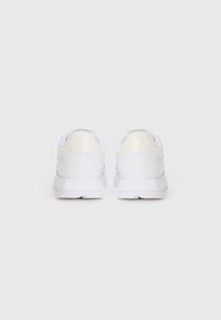 White athletic shoes with a smooth leather finish, padded collar, and minimalistic design. Features subtle cream accents on the heel.
