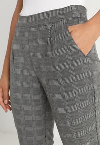 Šedé a černé kárované kalhoty z texturované látky, s bočními kapsami a střihovým střihem s předními záhyby.