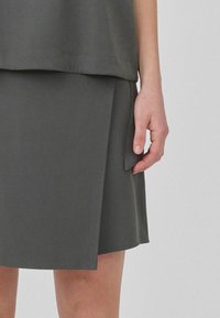 Szürke, laza szabású felső, kerek nyakkivágással, térd hosszúságú szoknyával párosítva, amely oldalán redőkkel és puha, sima textúrával rendelkezik.