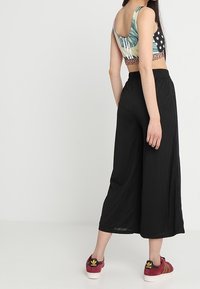 Pantalones anchos negros con un acabado texturizado, combinados con una camiseta corta de patrón multicolor. La modelo lleva zapatillas rojas y negras.