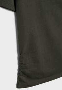 Mørkegrøn kortærmet skjorte, der viser stoftekstur og siderynke detalje nær kanten mod en lys baggrund.