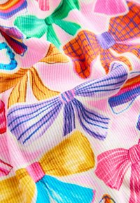 Buntes Gewebe mit auffälligen Schleifenmustern in Pink, Lila, Blau, Grün, Orange und Gelb auf einem gerippten Textur-Hintergrund.