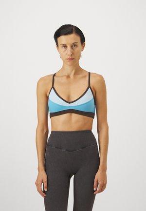 Sininen ja musta urheilibrasi, jossa on kolmiomainen muotoilu, säädettävät hihnat ja sileä pinta. Yhdistetty korkeavyötäröisten ribbileggingsejen kanssa, jotka ovat mustat.