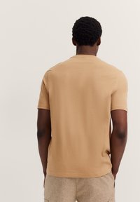 Short-sleeve, crew-neck t-shirt in light tan cotton. Simple design with smooth texture, featuring a straight hem and a relaxed fit.