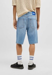 Shorts in denim azzurro chiaro con taglio dritto, dotati di due tasche posteriori e una vita con marchio. Indossati con sneakers nere e calzini a righe.