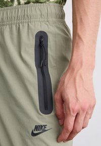 Light green athletic shorts feature a side zip pocket with black trim, elastic waistband, and a black Nike logo on the lower leg.