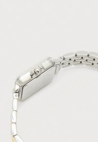 Strieborné kovové náramkové hodinky zobrazené z bočného uhla, s lesklou korunou a prepojeným náramkom na svetlom pozadí.