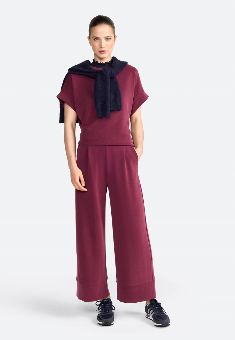Bordeauxfarbene Ko-Ord-Set mit kurzen Ärmeln und weit geschnittenen Hosen. Marineblauer Schal, der am Hals gebunden ist. Glatter Stoff mit lockerer Passform und Taschen.