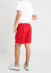 Röda idrottsshorts med elastisk midja och sidofickor, med en vit logotyp på vänstra benet. Bärs med en enkel vit t-shirt.