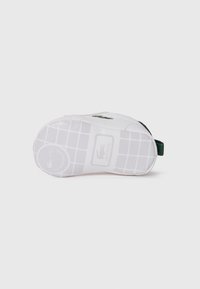 Sneaker bianco con suola in gomma testurizzata, dotata di un gancio posteriore verde e dettagli del logo discreti. Materiale superiore liscio con un design minimalista.