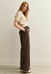 Beige wolmix korte mouwen trui gecombineerd met donkerbruin gestreepte wijde broek met een verstelbare koord taille. Witte schoenen.