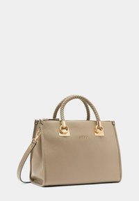 Sac à main en cuir beige avec des poignées supérieures tressées, des accents en matériel doré, un logo sur le devant et un design structuré. Inclut une bandoulière amovible.