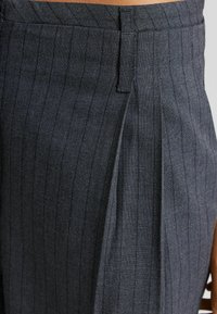 Mörkgrå plisserade byxor i texturerat tyg med vertikala ränder och dold framstängning för en ren finish.