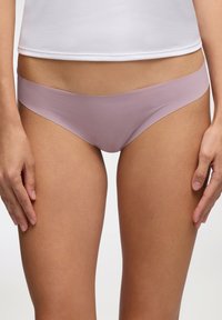 Mutande seamless rosa con una texture liscia, design a vita bassa e copertura minima. Indossate con una maglietta bianca, tenute con le mani sui fianchi.