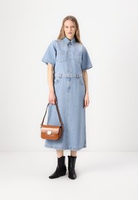 Denimová košilová šaty, světle modré, krátké rukávy, zapínání na knoflíky vpředu, dvě náprsní kapsy, páskový pas, ke kolenům. Černé kotníkové boty, hnědá kabelka.
