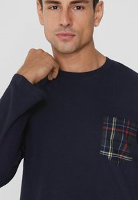 Granatowa koszula z długim rękawem z kieszenią w kratę w kolorach czerwonym, niebieskim i zielonym. Miękka tkanina i okrągły dekolt.