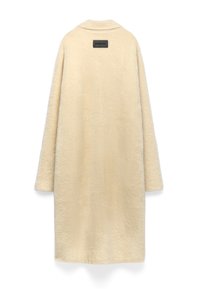 Lange beige nepbontjas met een eenvoudige kraag en een zwart rechthoekig label genaaid nabij de bovenrug.