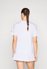 Weißes Baumwoll-T-Shirt mit kurzen Ärmeln, rundem Hals und lockerer Passform. Die Rückseite zeigt eine geflochtene Frisur und minimalistische Designelemente.