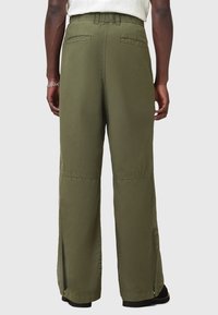 Pantalons large olive vert avec une texture lisse et légère, dotés de poches arrière et de fentes sur l'ourlet pour un détail supplémentaire.