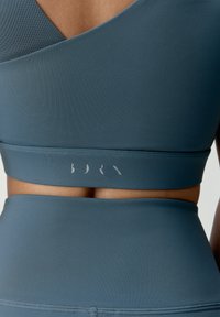 Svetlomodrá športová podprsenka s hladkou textúrou, s prekríženým dizajnom a jemným logom na páse.