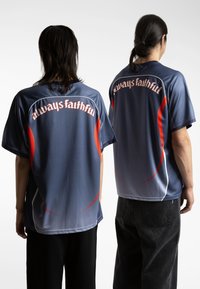 Īsām piedurknēm, zils sintētisks krekls ar sarkanām akcentiem un tekstu "vienmēr uzticīgs" uz aizmugures, brīvā piegriezumā un apaļā kakla izgriezumā.