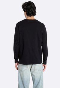 Zwarte longsleeve t-shirt met ronde hals, gemaakt van zachte stof. Heeft een eenvoudig ontwerp zonder patronen, gedragen met lichtblauwe jeans.