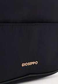Musta kangaskassi, jossa on sileä pinta, kultasävyinen "GIOSEPPO"-logo ja minimalistinen muotoilu. Yksinkertainen ommel reunoilla.