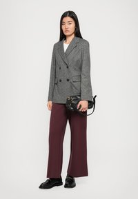 Blazer gris à double boutonnage avec une finition texturée, associé à un pantalon bordeaux large et des chaussures noires. Les accessoires comprennent un petit sac noir.