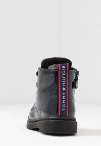 Tmavě modré lakované kozačky po kotníky s texturovaným povrchem, červeným a námořnickým pruhovaným logem a bočním zipem. Gumová podrážka pro lepší přilnavost.