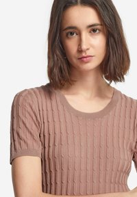 Ljusrosa stickad kortärmad tröja med en texturerad ribbmönster och rundad halsringning, tillverkad av ett mjukt, elastiskt material.