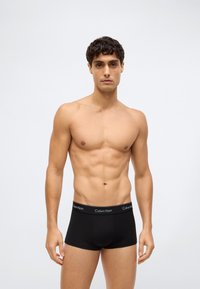 Černé bavlněné boxerky s měkkým elastickým pasem s logem "Calvin Klein". Model má vypracovanou postavu a krátké kudrnaté vlasy.