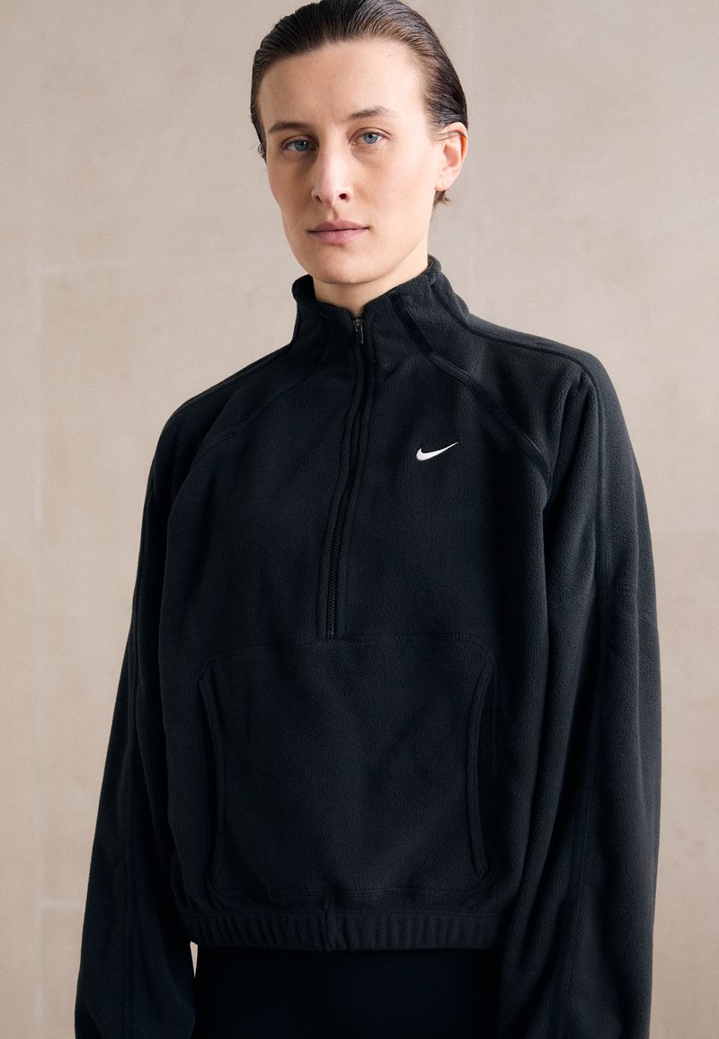 Pullover in pile nero con colletto alto, apertura a mezza zip frontale e tasca frontale. Presenta un piccolo logo bianco di Nike sul lato sinistro del petto.