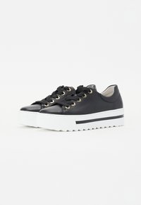 Svarte lær plattformsneakers med rund tå, svarte snøringer, gulløyler og hvit rillet såle med en svart aksentstripe.