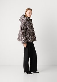 Chaqueta tipo plumón con un patrón de leopardo, capucha y corte oversized, combinada con pantalones negros de pierna ancha y zapatos negros de punta.