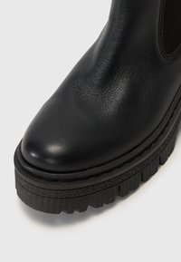 Juodas odinis kulkšninis botas su apvaliu pirštu, tekstūruota viršutinė dalis, elastiniai šoniniai paneliai ir storas, grioveliuotas juodas guminis padas.