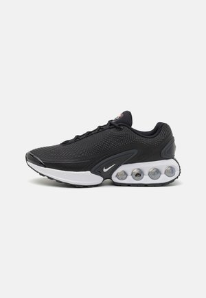 Baskets de sport noires avec une tige en mesh, une semelle intermédiaire blanche et des capsules de amortissement distinctives sur la semelle. Logo Nike sur le côté.