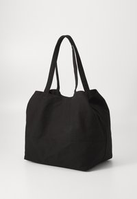 Black canvas tote bag with long, flat handles. Soft texture and spacious design, featuring side seams and a wide opening for easy access.
