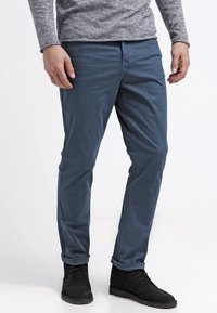 Donkerblauwe chino's van zacht, lichtgewicht stof, met een slim fit, achterzakken en een gladde structuur. Gecombineerd met zwarte enkellaarsjes.