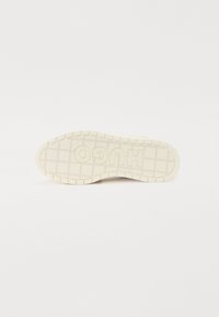 La semelle de la chaussure est de couleur crème avec le texte "HUGO" en relief. Un motif de grille texturé et des bords arrondis améliorent l'adhérence et la stabilité.