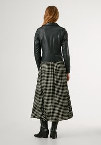 Jaqueta de couro preta com um design ajustado. Combinada com uma saia longa xadrez preto e branco e botas pretas até ao joelho.