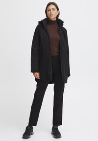 Black waterproof jacket with a hood, front zipper, and two side pockets. Paired with black pants and black footwear. Smooth texture overall.