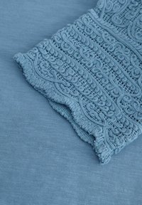 Light blue fabric featuring intricate lace detailing at the edge, with a textured finish and soft, woven appearance.
