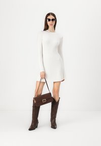 Robe en maille côtelée blanche à manches longues, sac à main marron avec une boucle rectangulaire, et bottes marron jusqu'aux genoux avec un motif en relief.