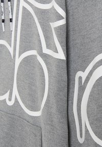 Felpa grigia con grande design grafico bianco. Presenta polsini a coste, cappuccio con cordino e una tasca a marsupio frontale. Texture morbida.