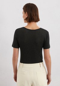 T-shirt nera a maniche corte con vestibilità comoda e scollatura ampia, abbinata a pantaloni crema a vita alta con tasche posteriori.