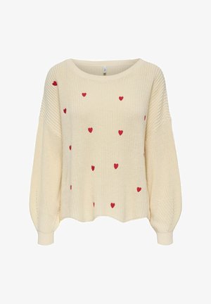 Kermainen neulepusero, jossa on pitkät pallohihat ja hajallaan pieniä punaisia sydänkuvioita edessä ja hihoissa.