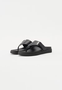 Sorte flip-flop sandaler med matt finish, minimalistisk design, bred stropp, tåpost og en liten metallaccent på stroppen.