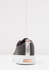 Černé tenisky s texturovaným materiálem. Mají metalickou stříbrnou patu a bílou podrážku. Na patě je značka s růžově zlatými akcenty.