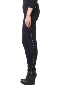 Vaqueros skinny azul marino con acentos de tachuelas doradas a lo largo de las costuras laterales, hechos de un material de denim elástico. Se llevan con botas de tobillo de cuña negras.