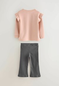 Svetloružový dlhý rukáv so stiahnutými ramenami v kombinácii s tmavosivými zvonovými nohavicami, oboje vyrobené z mäkkého, elastického materiálu.